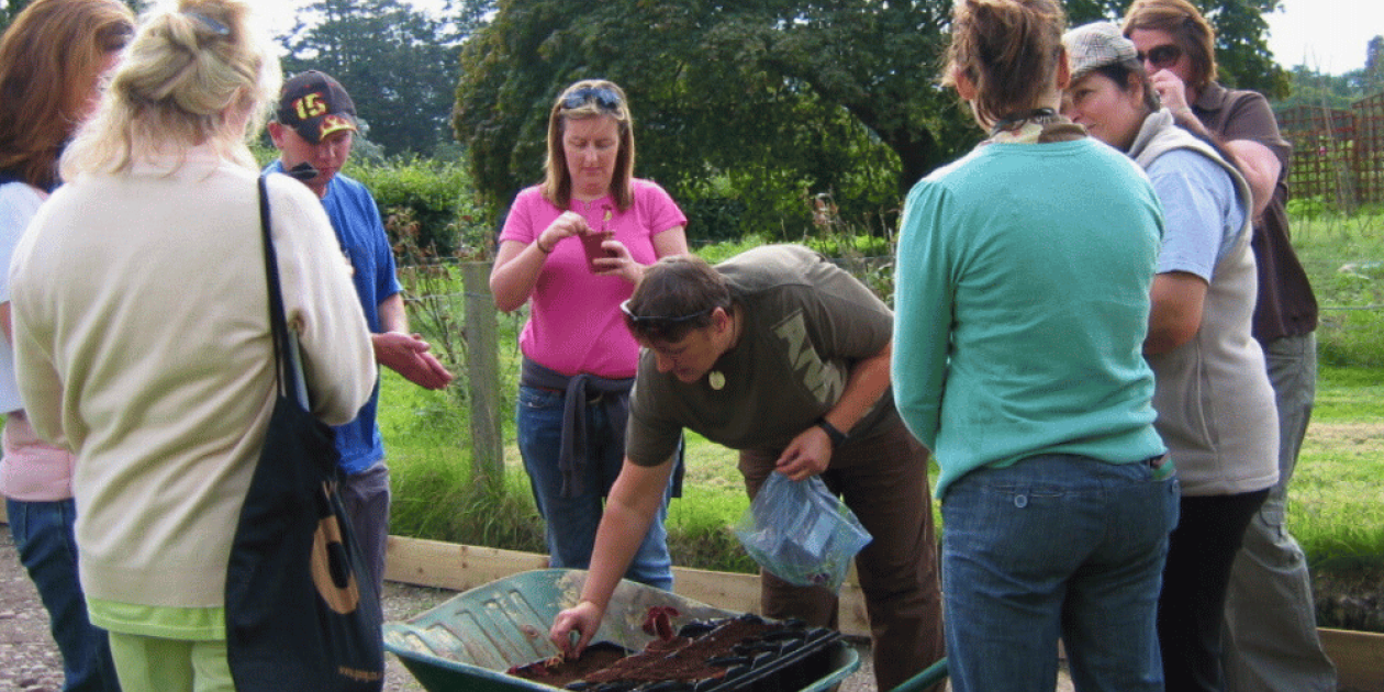 4 people gathered round a wheelbarrow , listening 