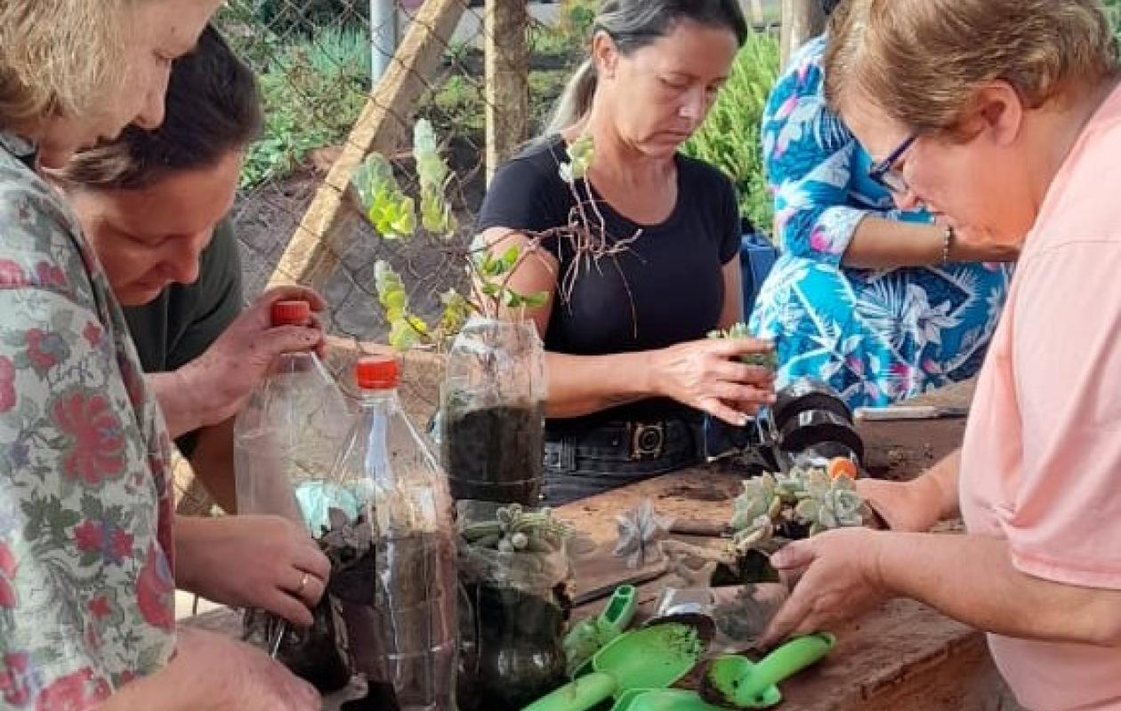 five people gathered around outdoor table handling pot plants and compost
